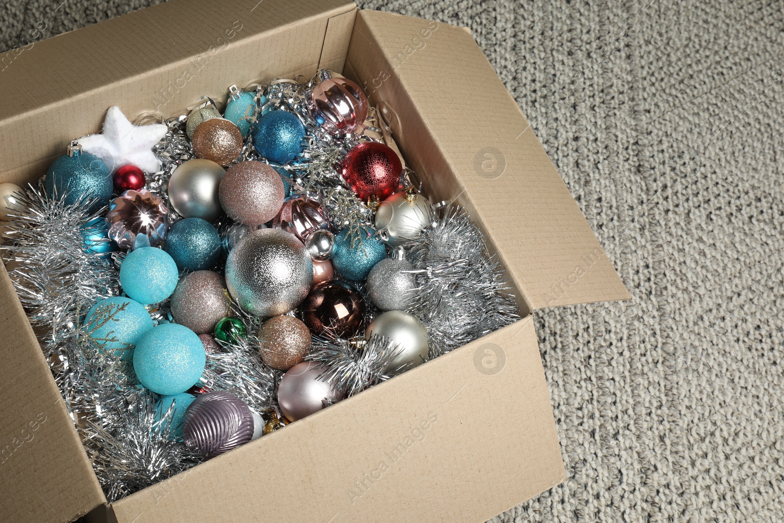 Photo of Different Christmas decor in cardboard box on carpet indoors