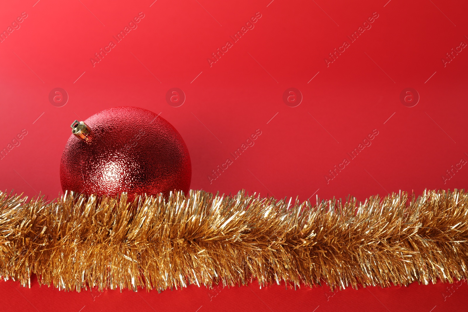 Photo of Beautiful Christmas ball and shiny tinsel on red background, space for text