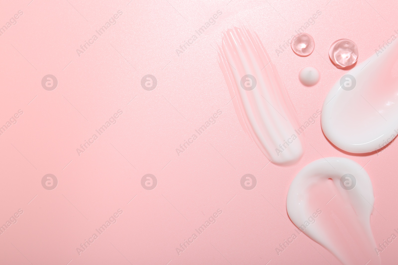 Photo of Cream and gel samples on pink background, top view. Space for text