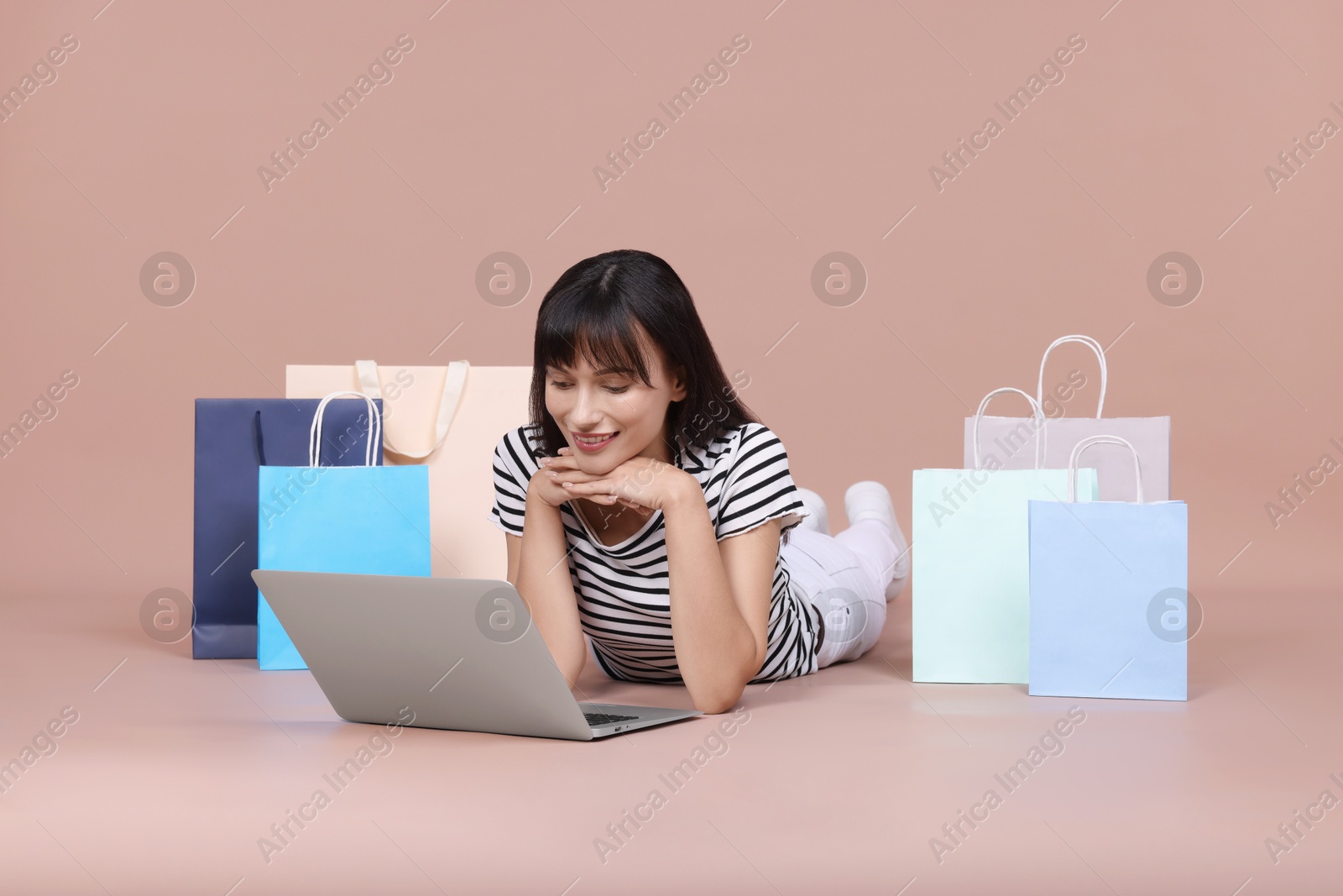 Photo of Internet shopping. Happy woman with laptop and colorful bags on beige background