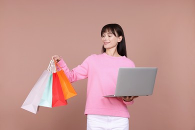 Photo of Internet shopping. Happy woman with laptop and colorful bags on beige background