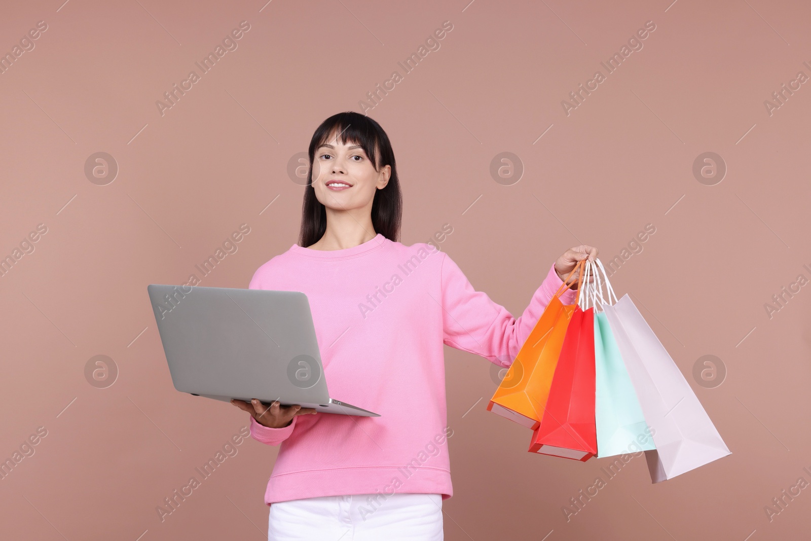 Photo of Internet shopping. Happy woman with laptop and colorful bags on beige background