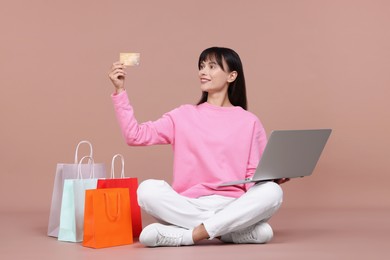 Photo of Internet shopping. Happy woman with credit card, laptop and colorful bags on beige background