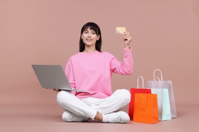 Photo of Internet shopping. Happy woman with credit card, laptop and colorful bags on beige background