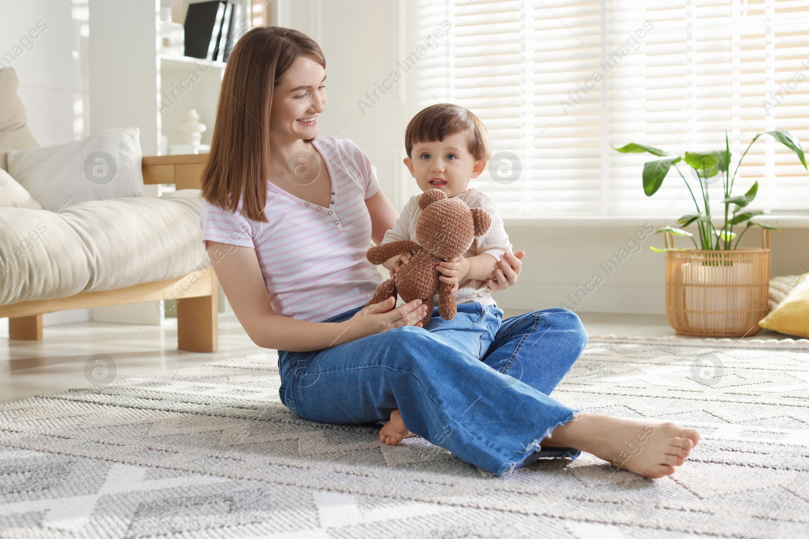 Photo of Happy mother and her cute little son with toy bear on carpet at home