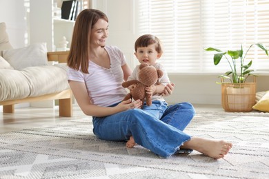 Photo of Happy mother and her cute little son with toy bear on carpet at home