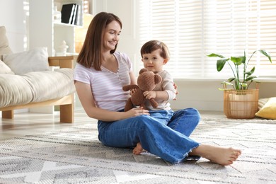 Photo of Happy mother and her cute little son with toy bear on carpet at home