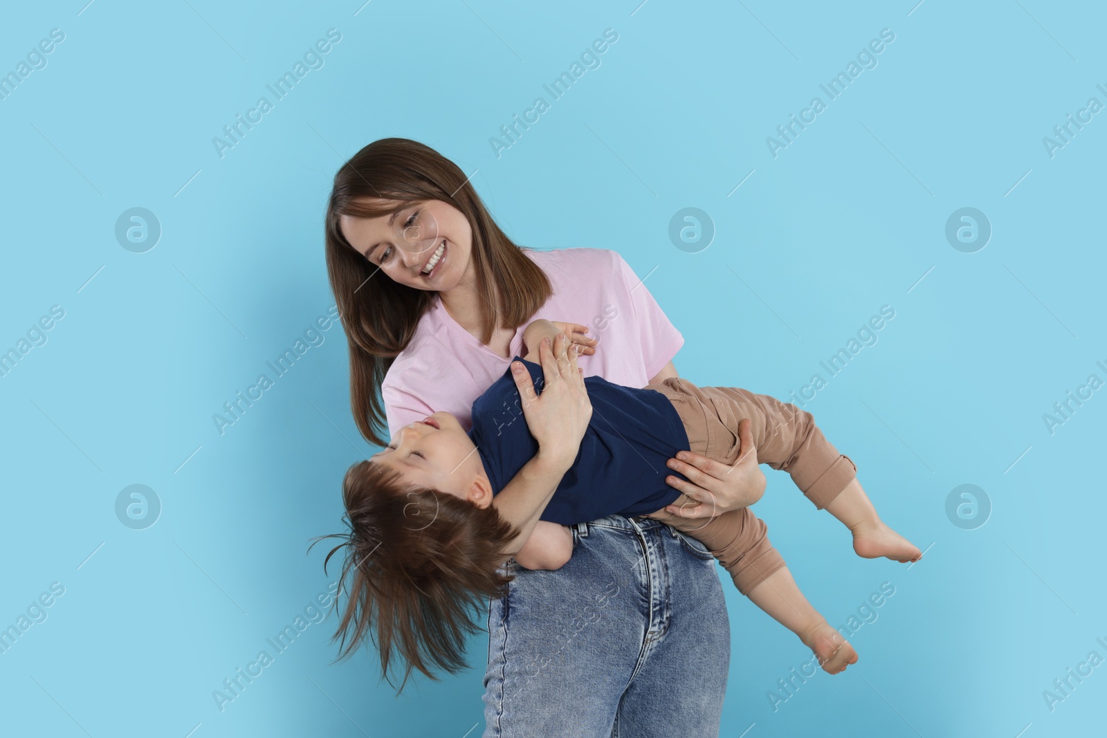 Photo of Happy mother having fun with her cute little son on light blue background