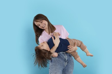 Photo of Happy mother having fun with her cute little son on light blue background