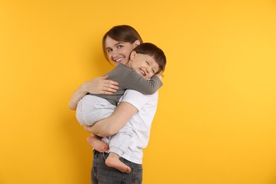 Photo of Happy mother with her cute little son on yellow background, space for text