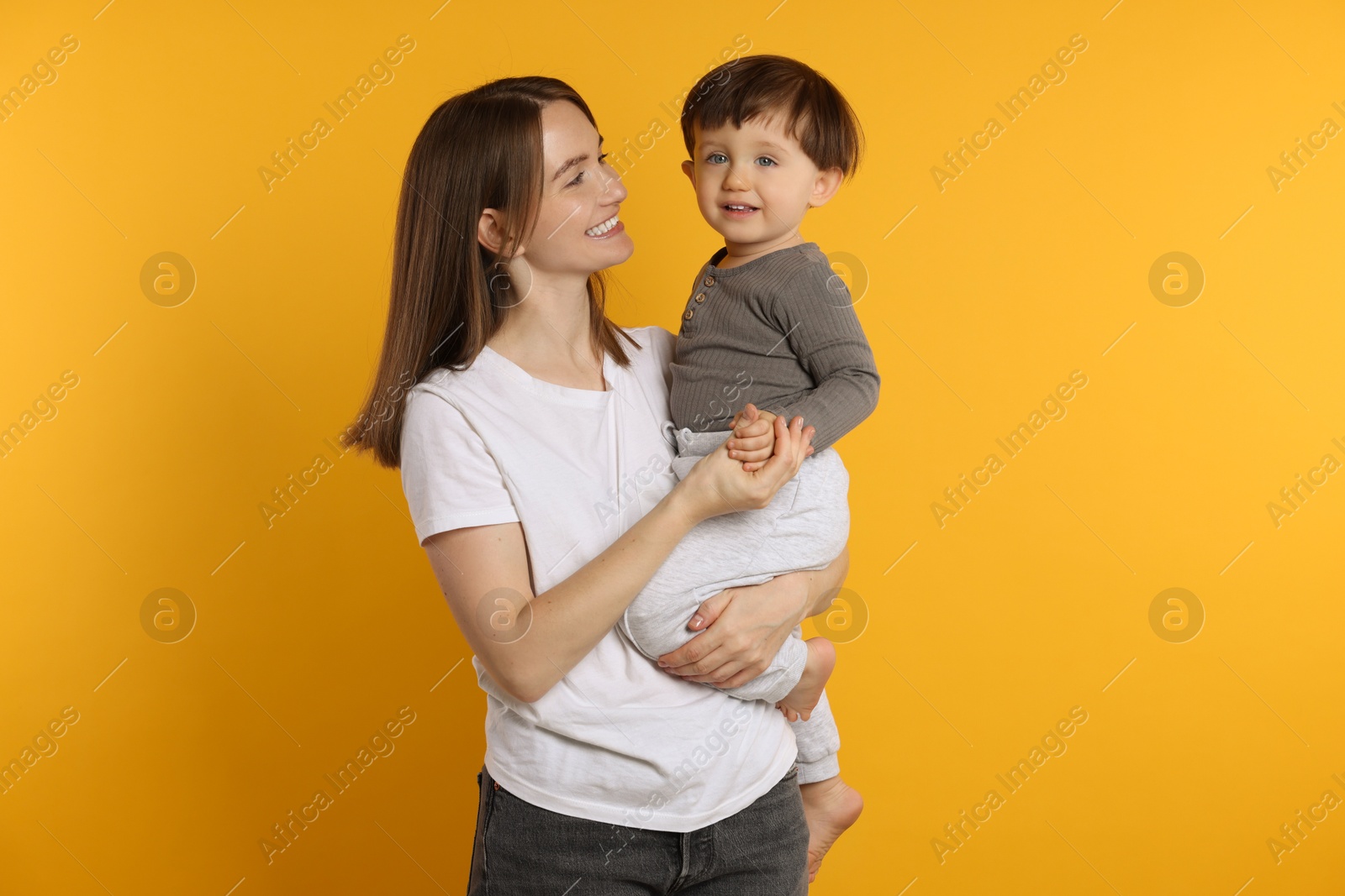 Photo of Happy mother with her cute little son on yellow background, space for text