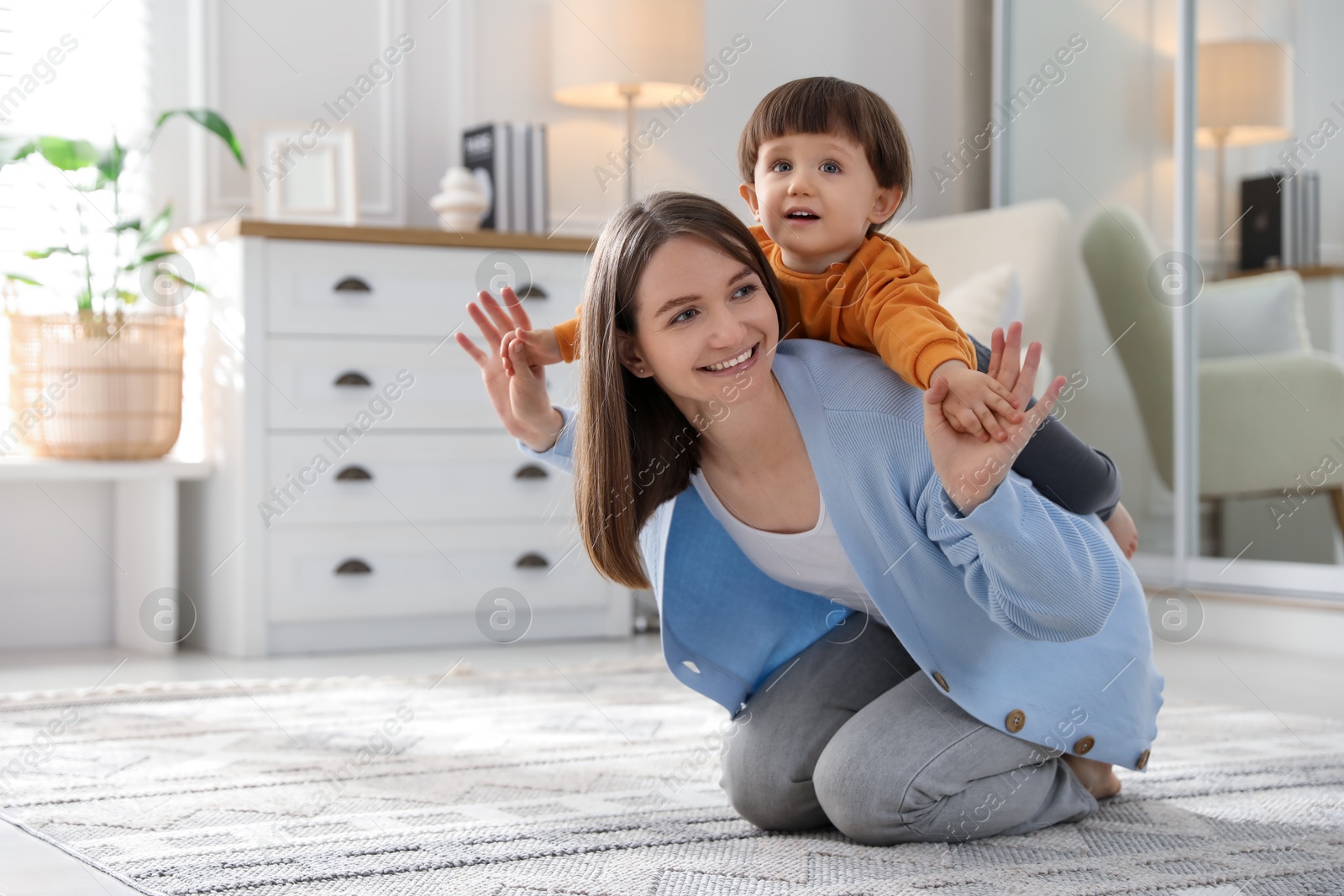 Photo of Happy mother playing with her little son at home. Space for text