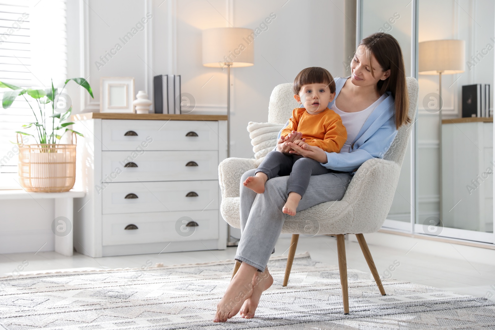 Photo of Mother with her little son sitting on armchair at home. Space for text