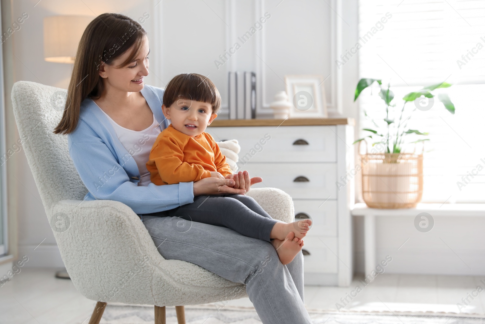 Photo of Happy mother with her little son sitting on armchair at home. Space for text