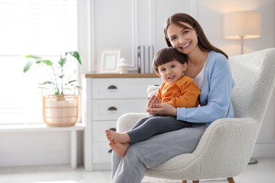 Photo of Happy mother with her little son sitting on armchair at home. Space for text