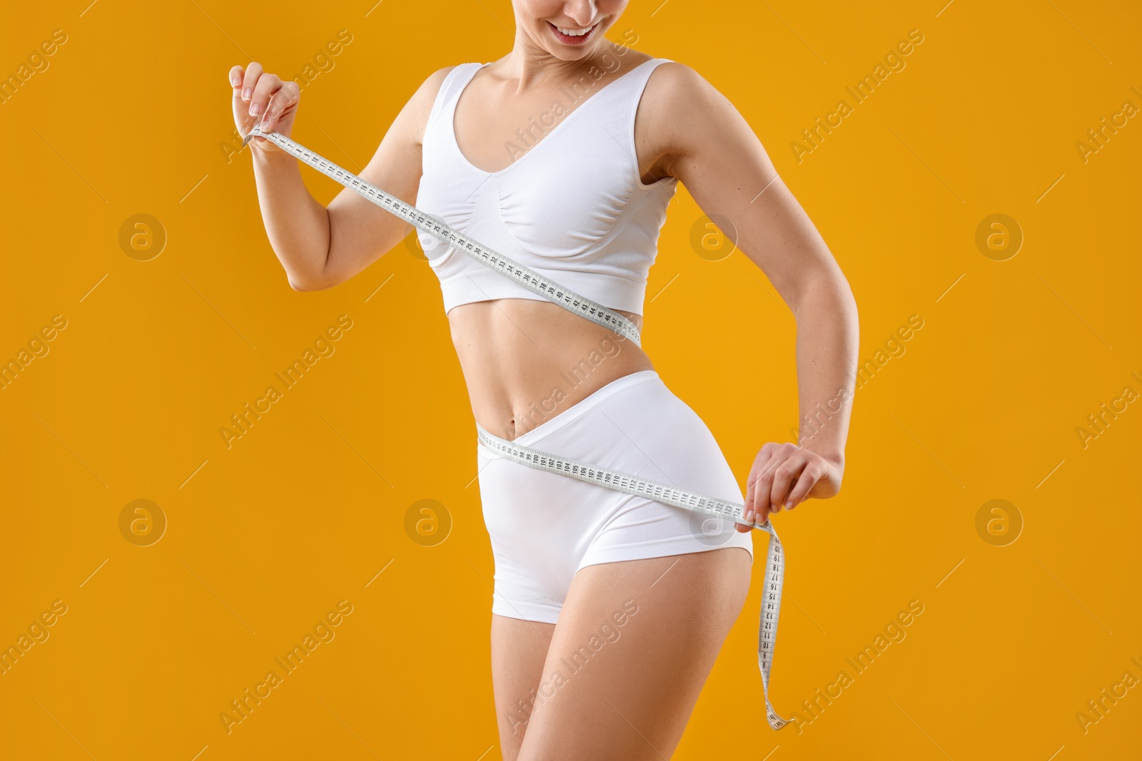 Photo of Weight loss. Woman measuring her slim waist with tape on yellow background, closeup