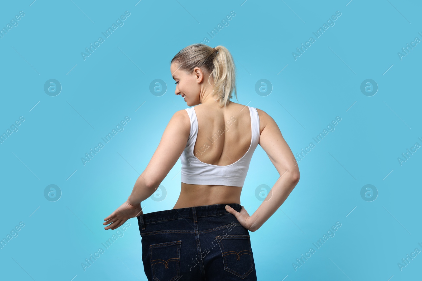 Photo of Weight loss. Happy woman wearing big jeans on light blue background