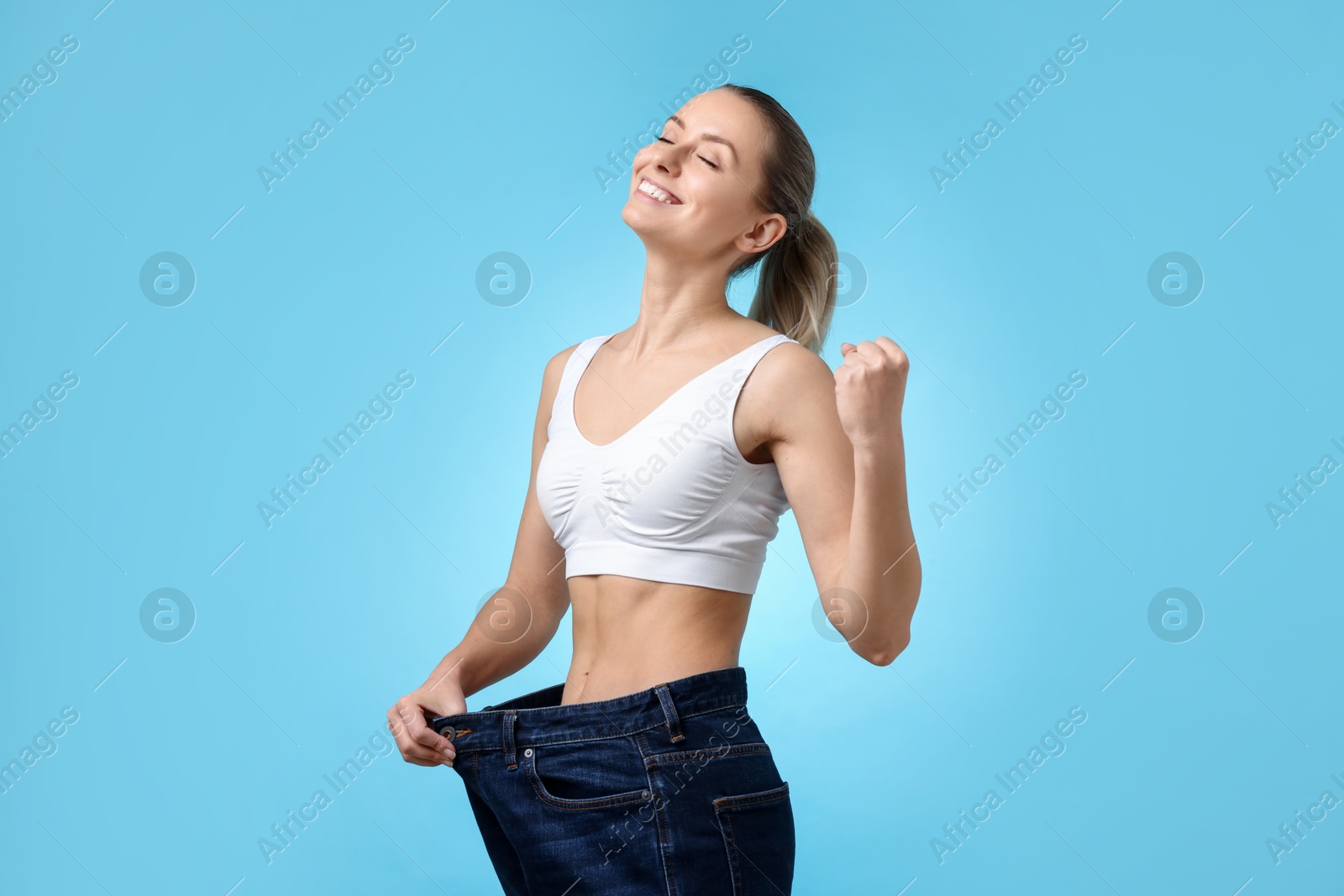 Photo of Weight loss. Happy woman wearing big jeans on light blue background