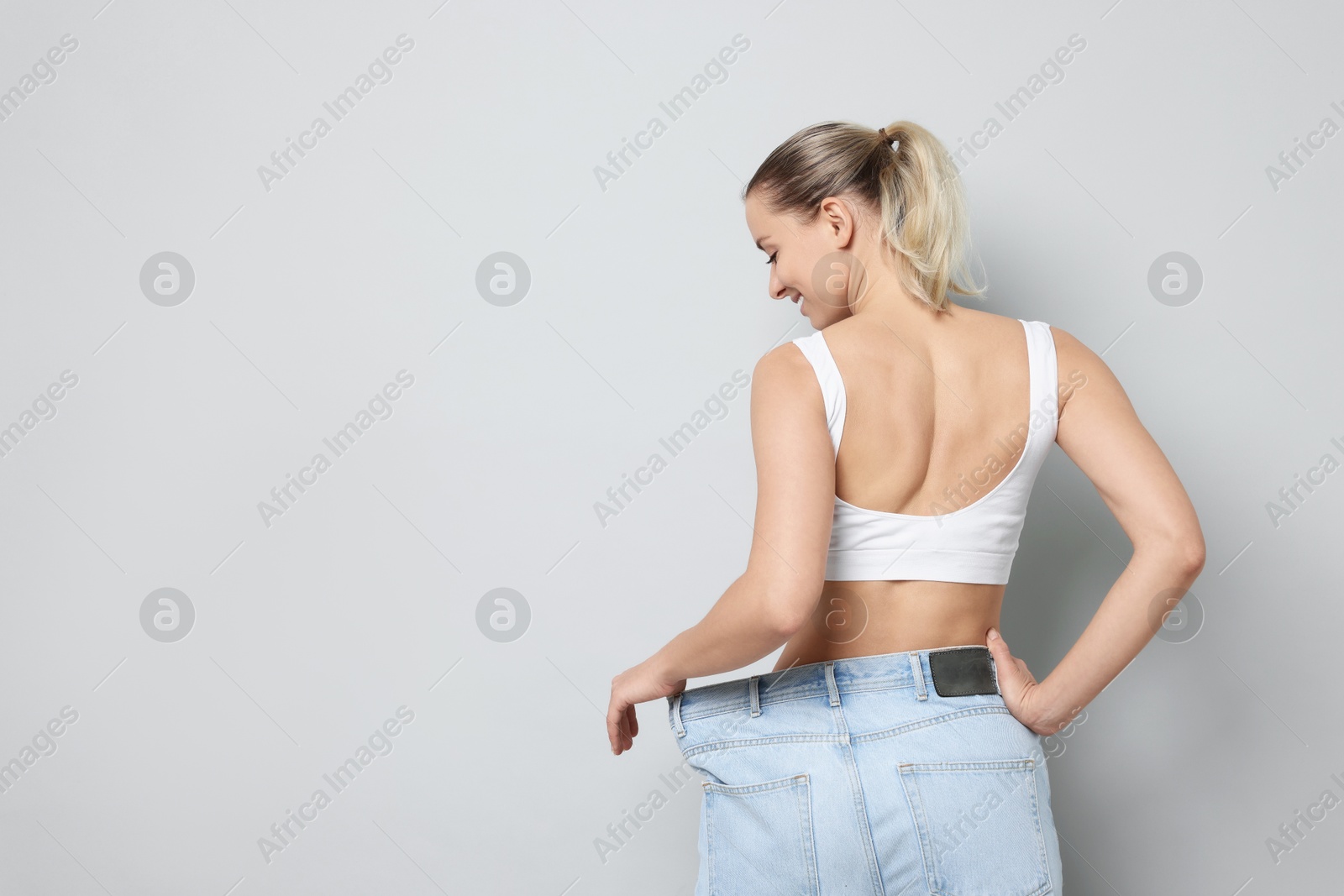 Photo of Weight loss. Happy woman wearing big jeans on light grey background, space for text