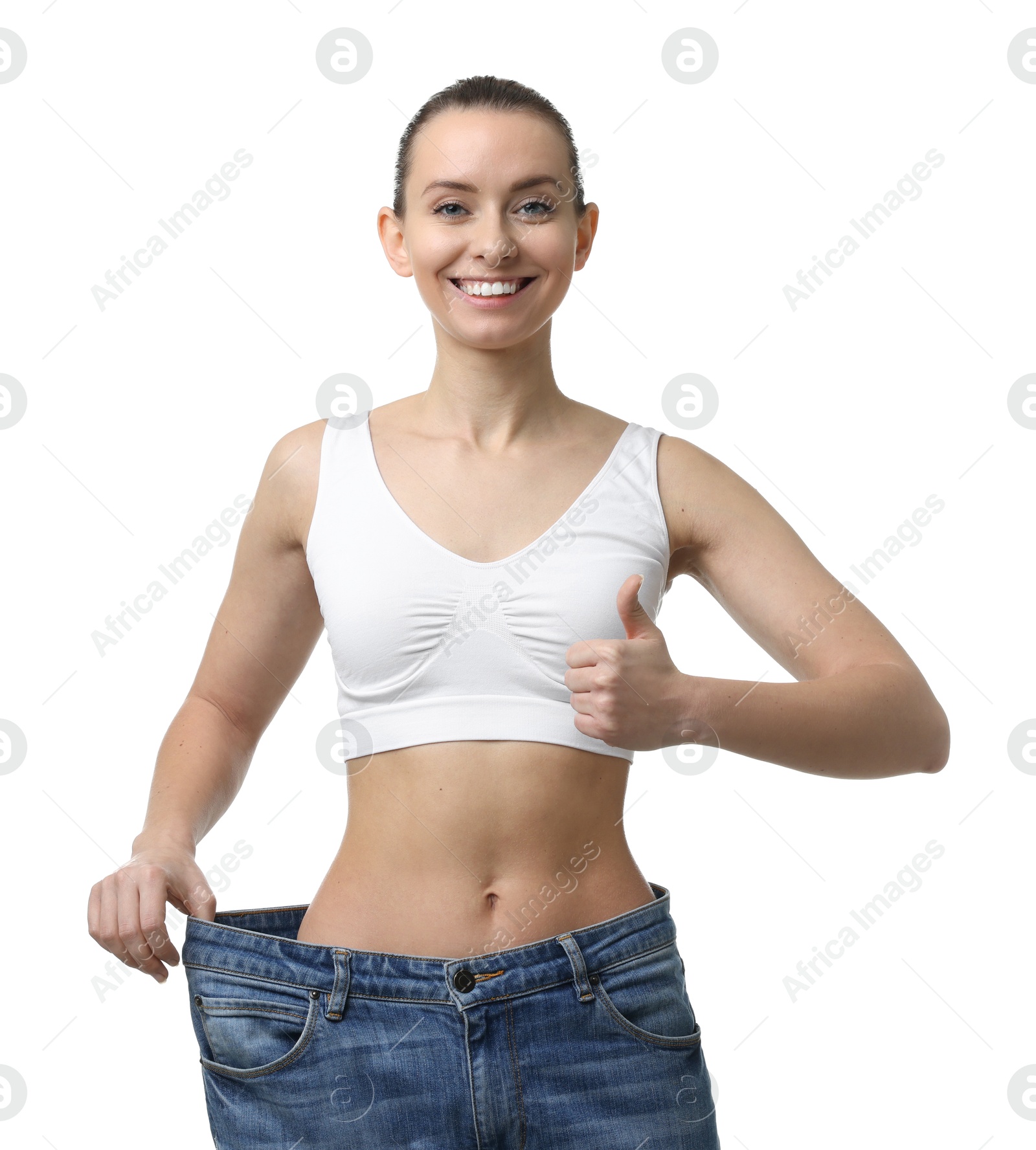 Photo of Weight loss. Happy woman wearing big jeans and showing thumbs up on white background