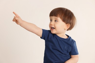 Photo of Cute little boy pointing at something on light grey background