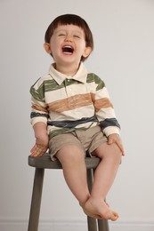 Photo of Emotional little boy sitting on stool against light grey background