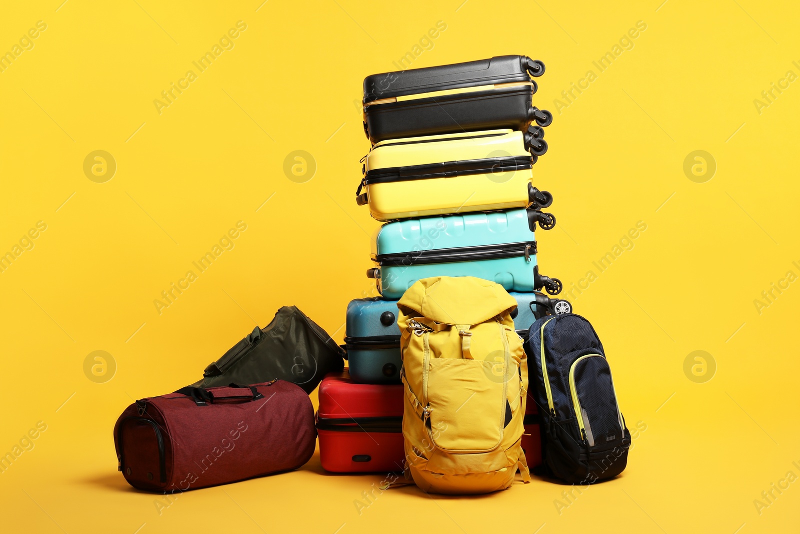 Photo of Stack of colorful suitcases, backpacks and bags on orange background