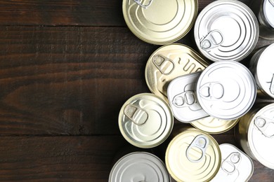 Photo of Many closed tin cans on wooden table, flat lay. Space for text