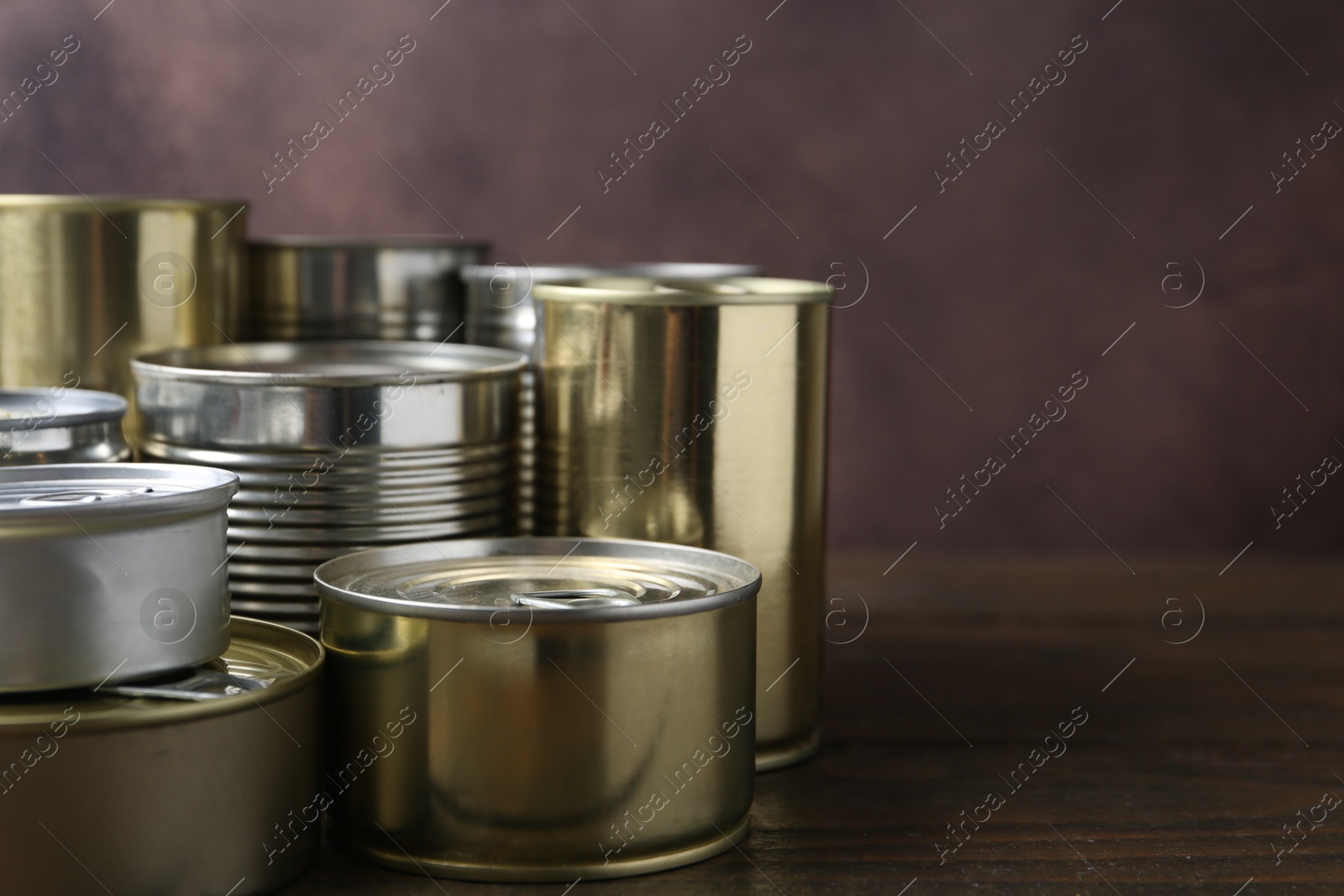 Photo of Many closed tin cans on wooden table, closeup. Space for text