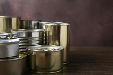 Photo of Many closed tin cans on wooden table, closeup. Space for text