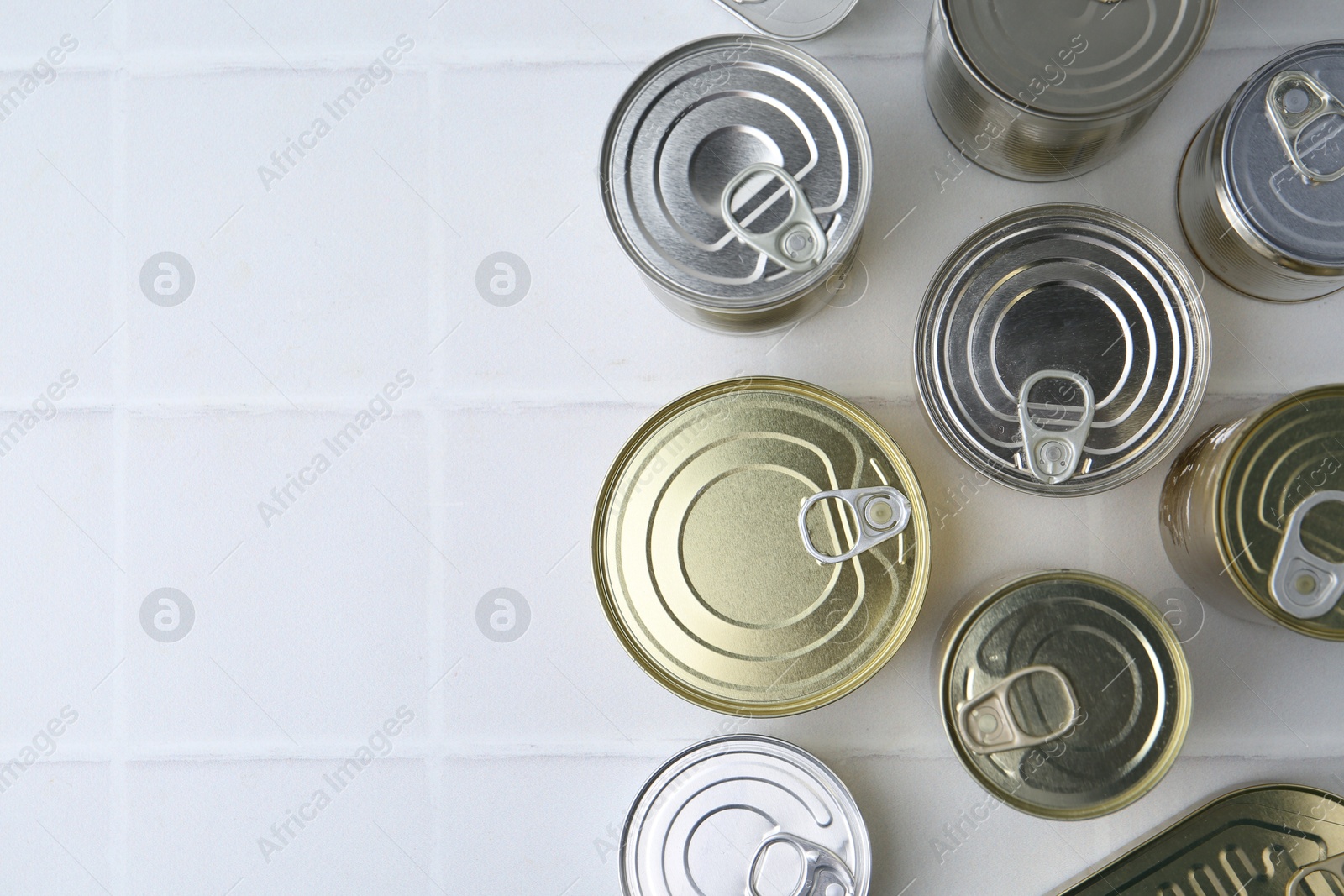 Photo of Many closed tin cans on white tiled table, flat lay. Space for text