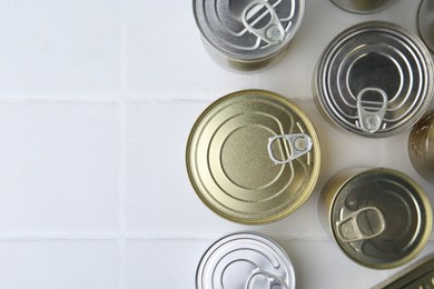 Photo of Many closed tin cans on white tiled table, flat lay. Space for text