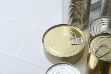 Photo of Many closed tin cans on white tiled table, closeup. Space for text