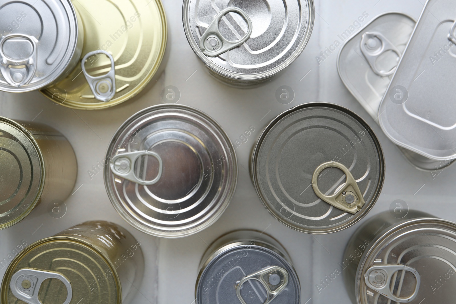 Photo of Many closed tin cans on white tiled table, flat lay