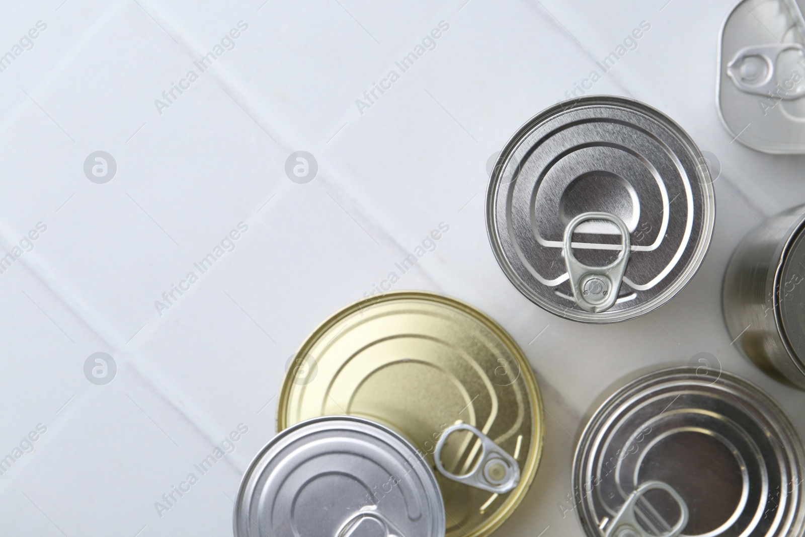 Photo of Many closed tin cans on white tiled table, flat lay. Space for text