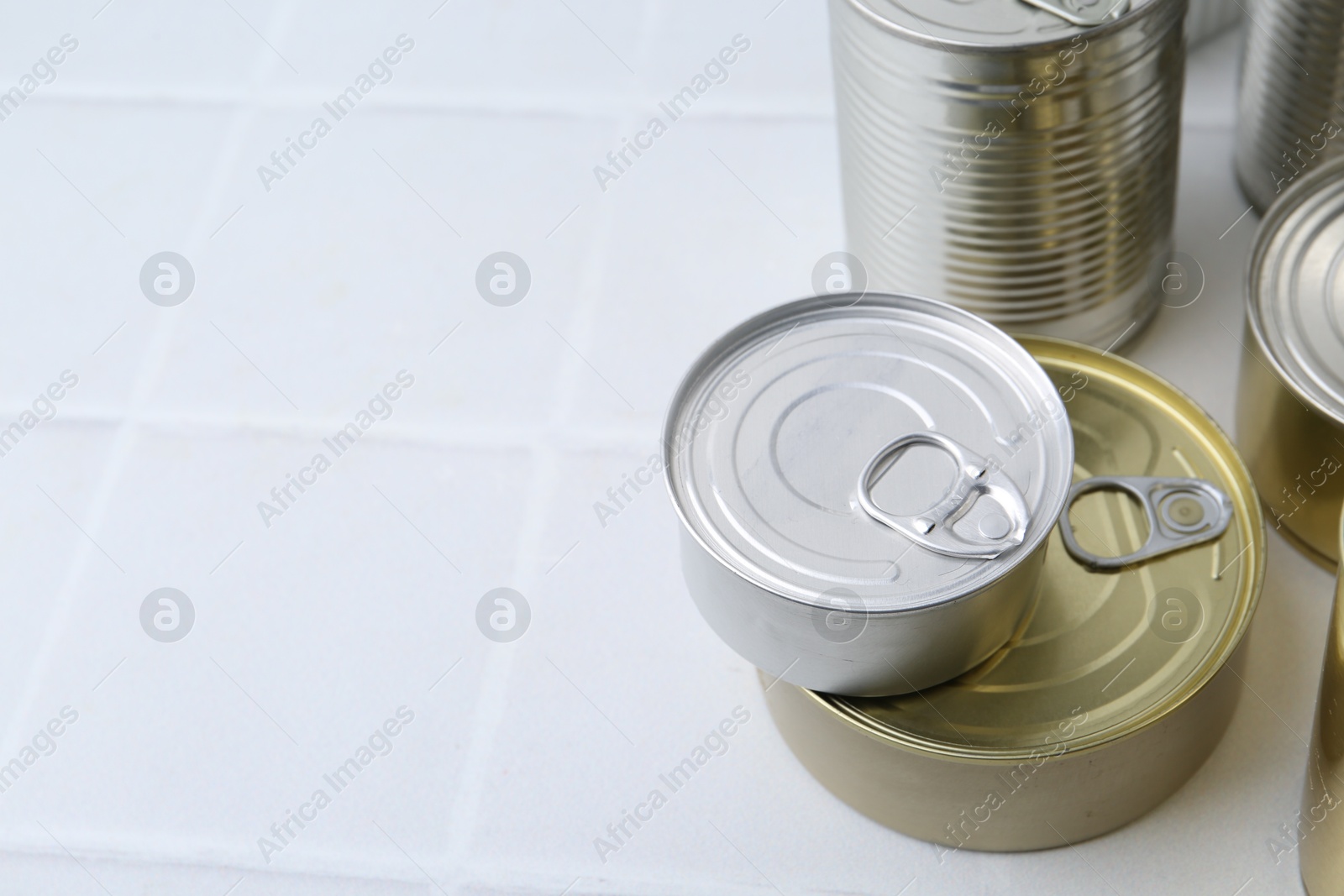 Photo of Many closed tin cans on white tiled table, closeup. Space for text