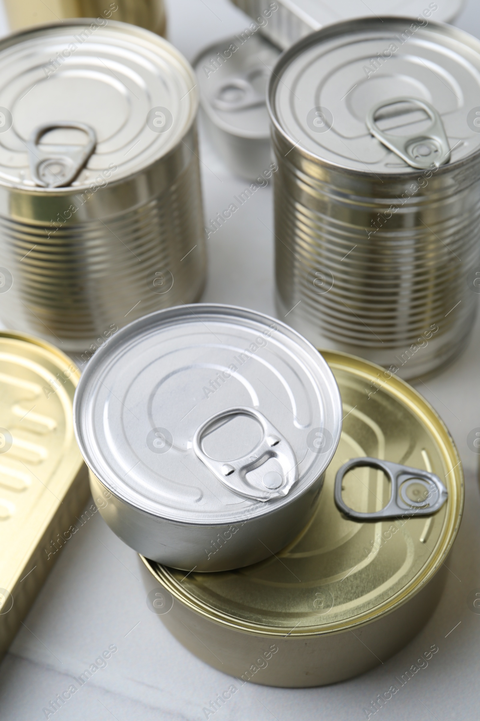 Photo of Many closed tin cans on white tiled table, closeup