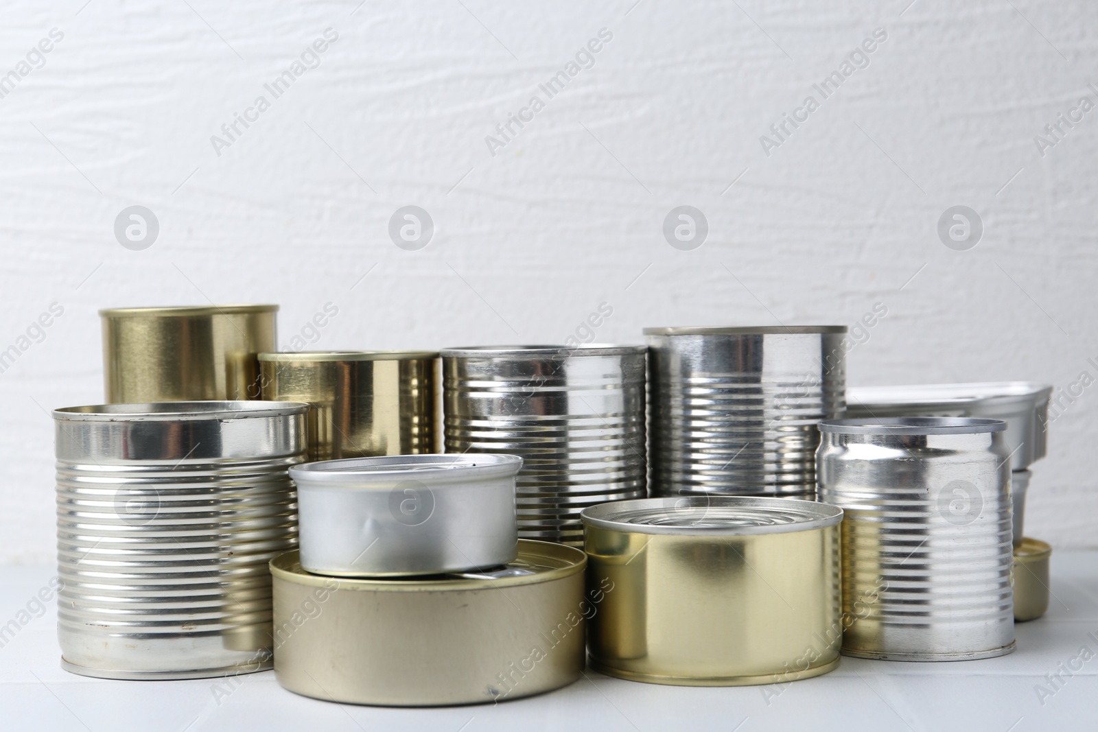 Photo of Many closed tin cans on white tiled table, closeup