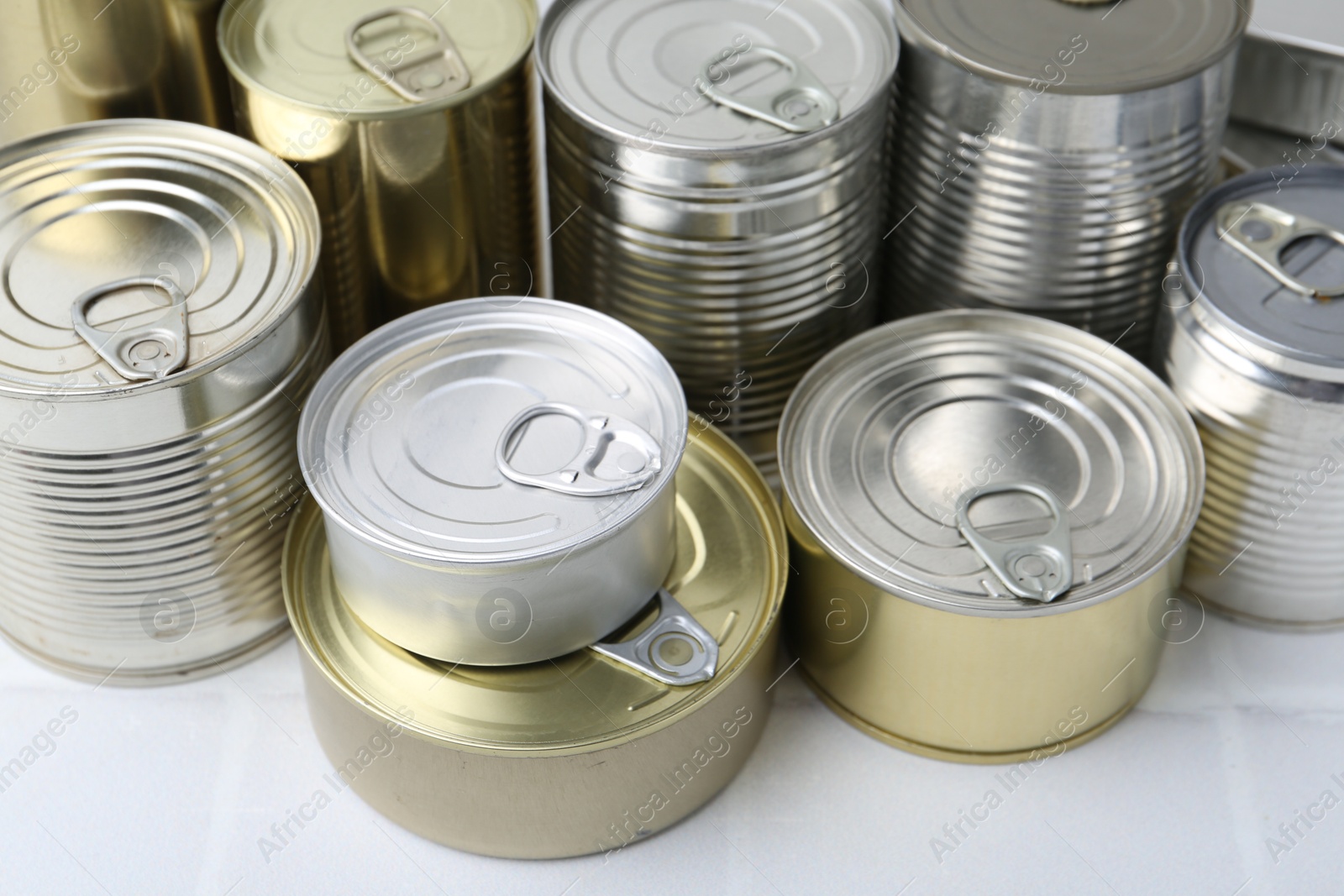 Photo of Many closed tin cans on white tiled table, closeup