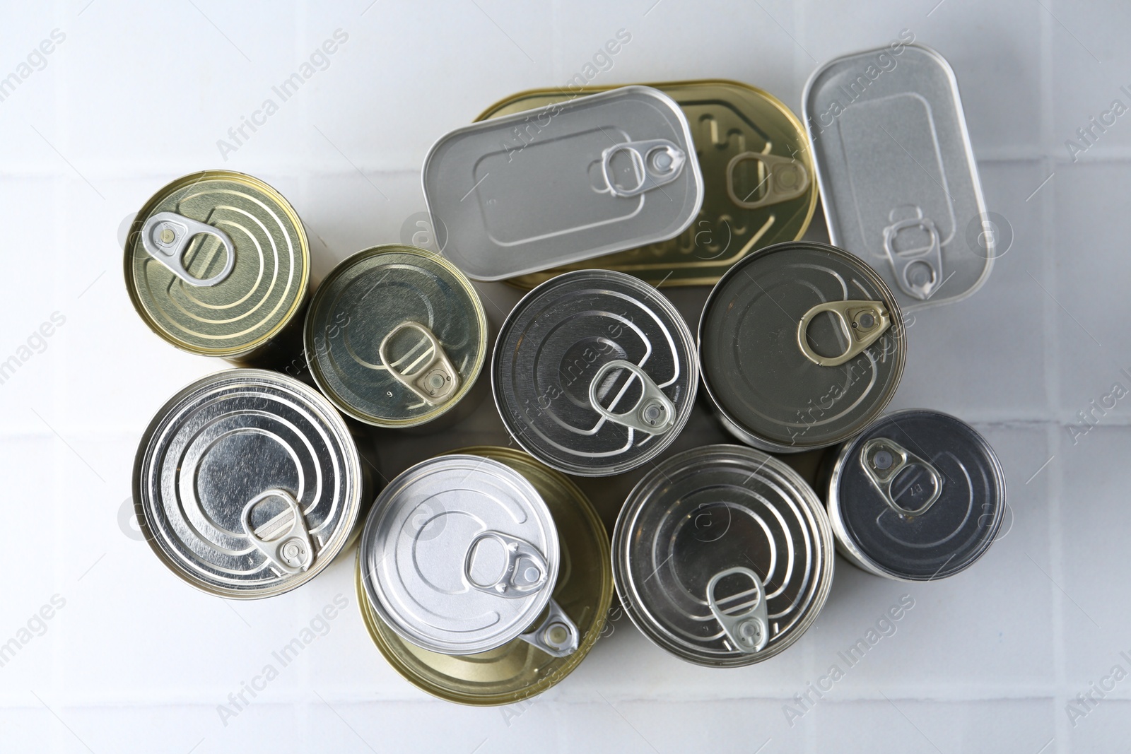 Photo of Many closed tin cans on white tiled table, flat lay