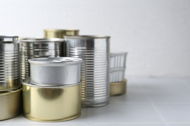 Photo of Many closed tin cans on white tiled table, closeup. Space for text