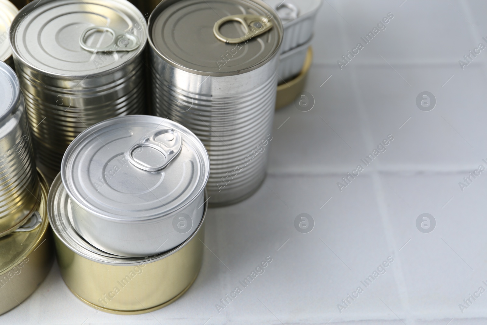 Photo of Many closed tin cans on white tiled table, closeup. Space for text