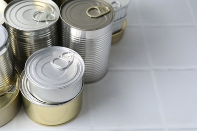 Photo of Many closed tin cans on white tiled table, closeup. Space for text