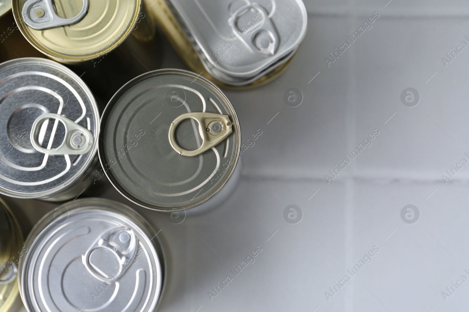 Photo of Many closed tin cans on white tiled table, flat lay. Space for text