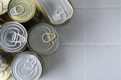 Photo of Many closed tin cans on white tiled table, flat lay. Space for text