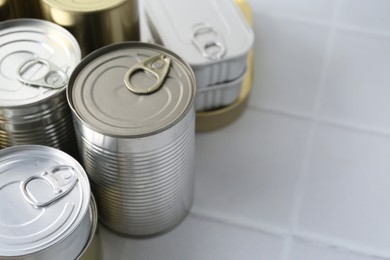 Photo of Many closed tin cans on white tiled table, closeup. Space for text