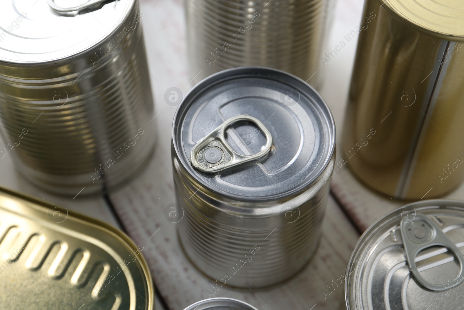 Photo of Many closed tin cans on white wooden table, closeup