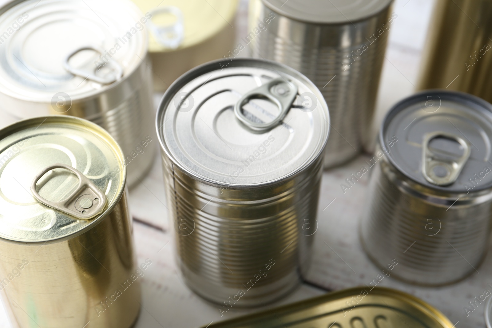 Photo of Many closed tin cans on white wooden table, closeup