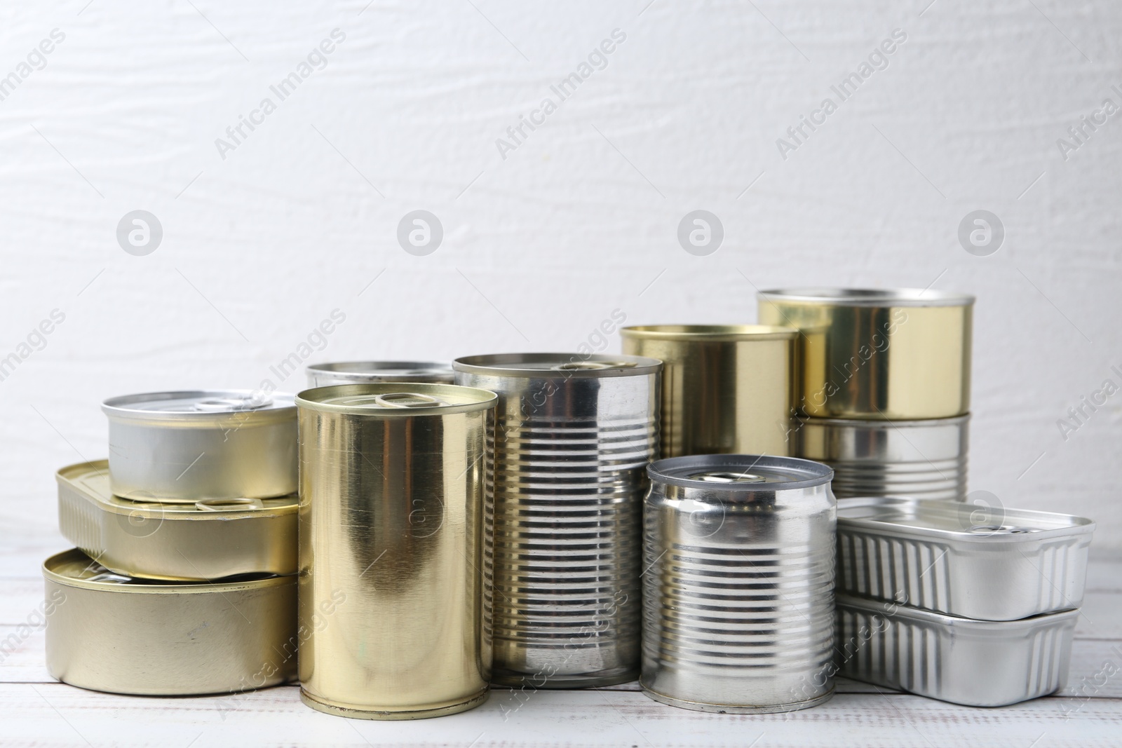 Photo of Many closed tin cans on white wooden table, closeup