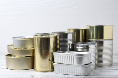 Photo of Many closed tin cans on white wooden table, closeup